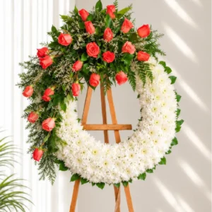 Corona Fúnebre Memoria circular de crisantemos blancos con rosas color coral en la parte superior, sobre atril de madera.