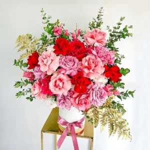 Ramo de rosas rojas y rosadas para expresar amor Ramo de flores con rosas rojas y rosadas, follaje verde y dorado en base blanca elegante, ideal para expresar amor y admiración.