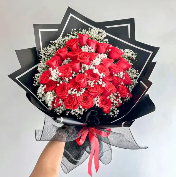 Ramo Buchón de rosas rojas con gypsophila blanca, diseño elegante con papel negro y lazo rojo vibrante.